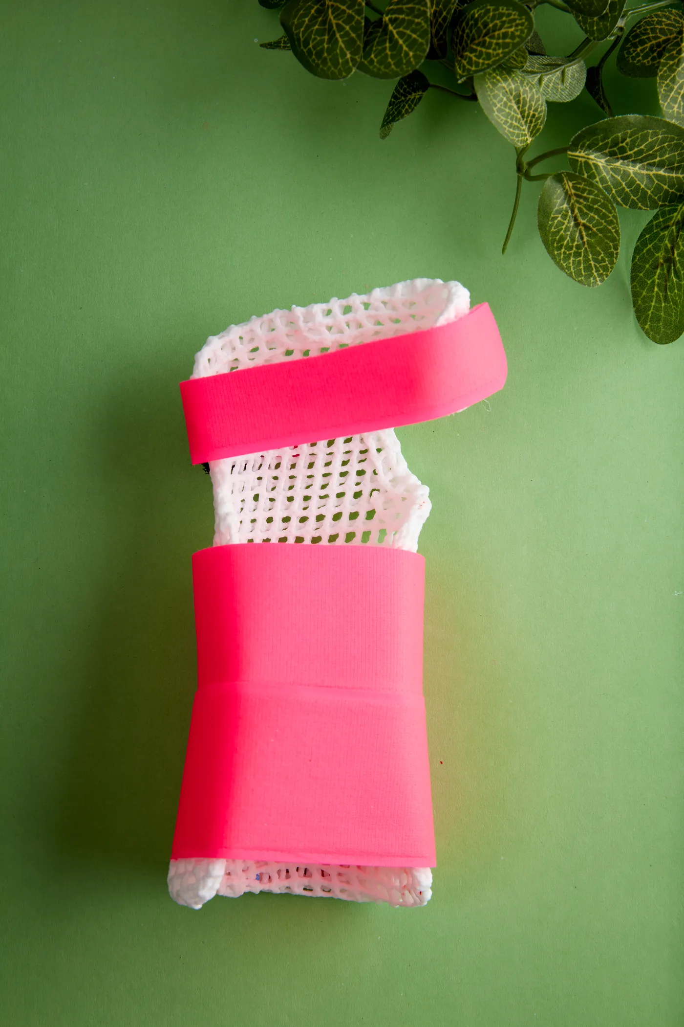 Tutore per polso in X-Lite Plus bianco con fasce rosa fluo, su fondo verde